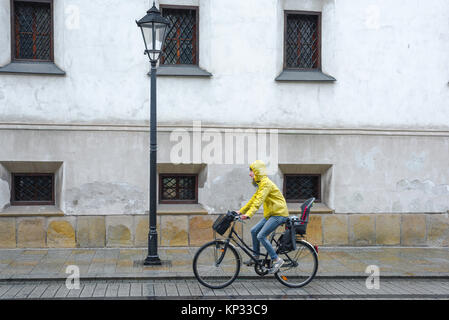 Frau, die Regen radeln, Blick auf eine Frau, die einen gelben Anorak trägt, der durch einen Regenguss in der Grodzka Straße, Krakow, Polen, radeln kann. Stockfoto