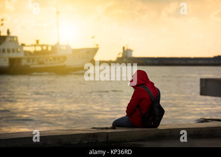 Einsame Mädchen sitzt am Hafen Stockfoto