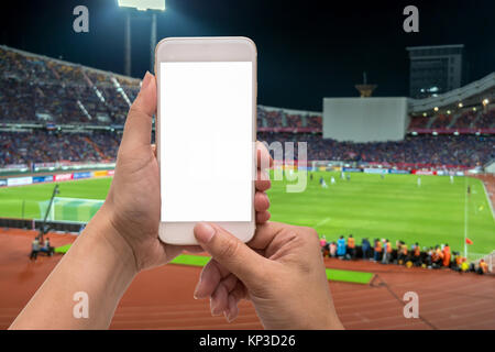 Weibliche Hand, die eine Mobile Smartphone Touchscreen auf der Fotograf, Foto bei Player in abstrakten verwischt verschwommenes Foto von Fußball-stadi Stockfoto