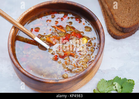 Peruanische Suppe mit Quinoa, roter Reis und Linsen in eine hölzerne Schüssel mit Kräutern und Roggenbrot. Gesunde vegane Ernährung Konzept. Stockfoto