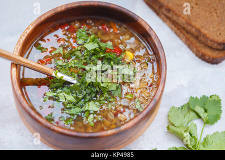 Peruanische Suppe mit Quinoa, roter Reis und Linsen in eine hölzerne Schüssel mit Kräutern und Roggenbrot. Gesunde vegane Ernährung Konzept. Stockfoto