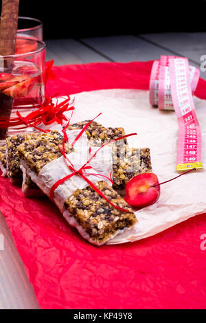 Diät Müsliriegel mit detox Apfel-zimt-Wasser und Maßband auf rote Paprika und Holz- Hintergrund. Stockfoto