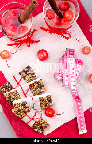 Diät Müsliriegel mit detox Apfel-zimt-Wasser und Maßband auf rote Paprika und Holz- Hintergrund. Ansicht von oben. Flach Stockfoto