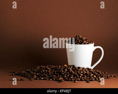 weiße Tasse umgeben von Kaffeebohnen auf Kaffee farbigen Hintergrund mit allerlei Textfreiraum Stockfoto