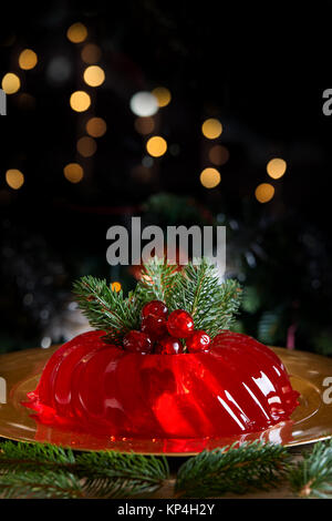 Rote Gelee für Weihnachten mit Tannenzweigen und kandierten Kirschen eingerichtet, auf dunklen Hintergrund mit Bokeh leuchtet. Stockfoto