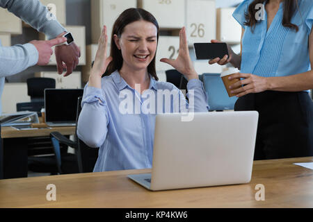 Kollege zeigt Zeit und Mobiltelefon zu frustrierten Frau im Büro Stockfoto