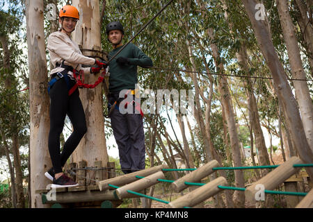 Portrait von lächelnden Paar hält Zip Line Kabel stehen auf hölzernen Plattform im Wald Stockfoto