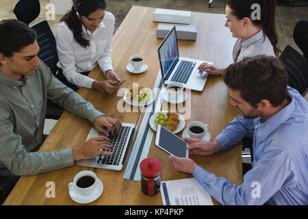 Gruppe von Führungskräften diskutiert mit Laptop und Snack am Schreibtisch im Büro Stockfoto