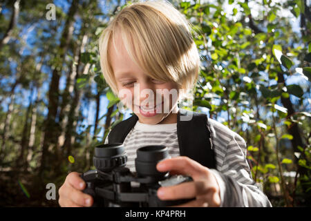 Kleines Mädchen mit Rucksack mit Fernglas in der Hand im Wald Stockfoto