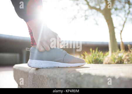 In der Nähe der weiblichen Jogger band ihre Schnürsenkel an einem sonnigen Tag Stockfoto