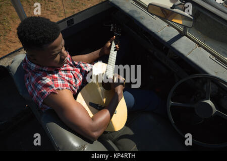 Mann spielt Gitarre im Auto an einem sonnigen Tag Stockfoto