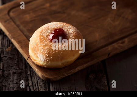 Nahaufnahme eines sufganiyah, eine jüdische Krapfen gefüllt mit Strawberry jelly traditionell gegessen auf Hanukkah, auf einem rustikalen Holztisch Stockfoto