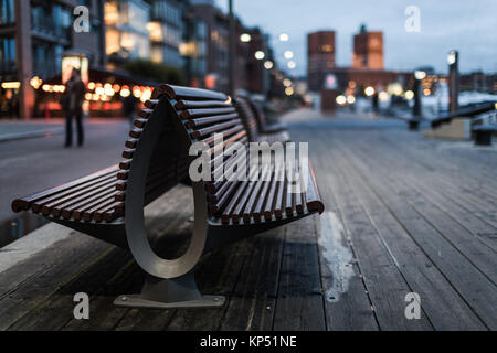 Eine Bank im Sonnenuntergang auf Aker Brygge in Oslo, Norwegen. Auf der Rückseite können Sie die City Hall. Aker Brygge ist eine beliebte Touristenattraktion in diesem europ Stockfoto