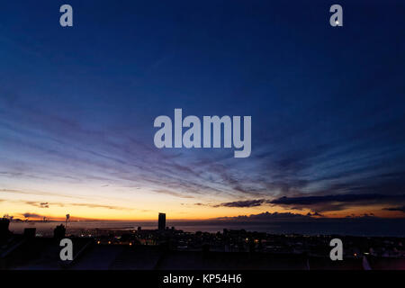 Ein Halbmond ist noch sichtbar in den klaren Himmel über Dächer während einer frühen eisigen Morgen in Swansea, Wales, UK. Dienstag, 12 Dezember 2017 Stockfoto