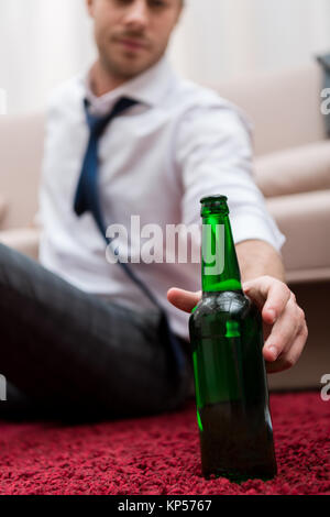 Mann die Flasche Bier, während er auf dem Teppich im Wohnzimmer Stockfoto