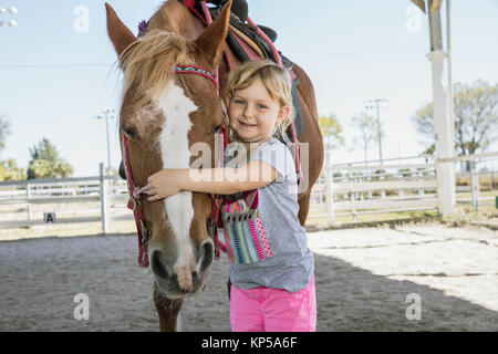 Schöne Mädchen ihr Pferd umarmte. Pferd und Jockey kleine süße kleine Mädchen in rosa Hosen mit einem Helm und Ihr bester Freund Stockfoto