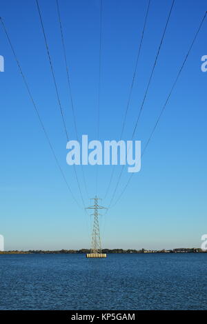 Power Transmission Turm in einem See vor einem strahlend blauen Himmel isoliert Stockfoto