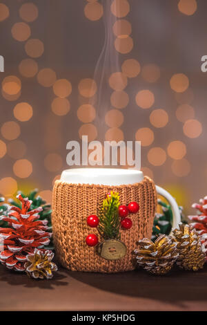 Nahaufnahme des Weißen dämpfen Winter Cup in Braun in Form gestrickter Pullover mit Weihnachtsschmuck auf hölzernen Tisch Stockfoto