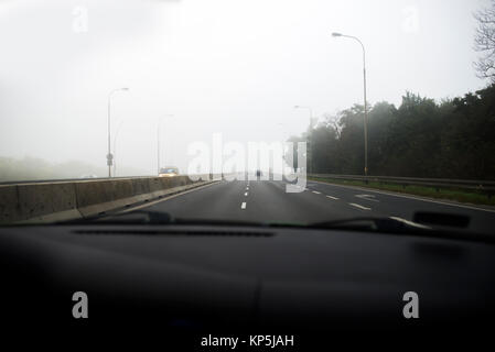 Auto fahren in dichtem Nebel, gesehen durch die Windschutzscheibe eines anderen Fahrzeugs Stockfoto