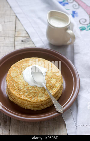 Stapel von russischen Pfannkuchen mit Sauerrahm - Blini auf einer Platte am Holztisch. Stockfoto