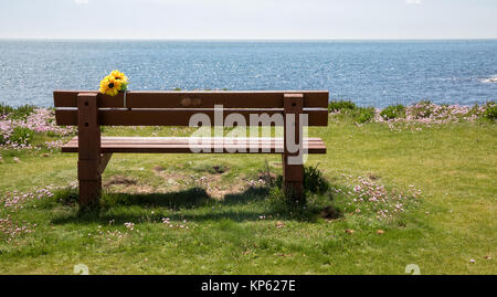 Leere Holzbank mit Blick auf den Ärmelkanal mit poignant Denkmal Blumen auf dem Küstenweg von Portland Bill in Dorset UK Stockfoto