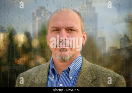 Ein Mann mit einem Schnurrbart und Bart sieht durch das Fenster, das im Regen beschlagenen hat, die Tropfen Stockfoto