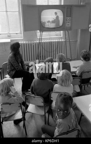 Grundschulkinder der 1970er Jahre schauen im Klassenzimmer fern. Schulfernsehen auf einem Stand, damit jeder sehen kann. Der Schullehrer sitzt vorne. Junge schwarze britische Mädchen, die sich umdreht, multiethnische England 1972 UK HOMER SYKES Stockfoto