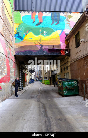 O'Keefe Lane Gasse mit vielen grünen Müll Müllcontainer aufgereiht an der Wand, man rauchen, Graffiti Artwork, Toronto, Ontario, Kanada. Stockfoto