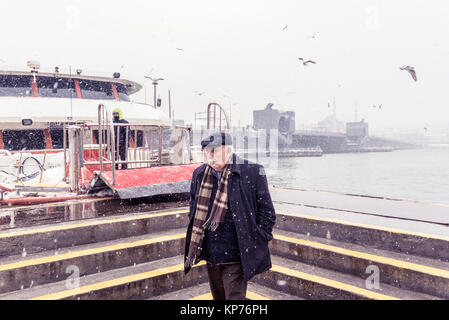 Unbekannter Mann zu Fuß in der Nähe von Karaköy Uskudar Pier an einem verschneiten Tag im Winter. Neue Moschee ist auf dem Hintergrund. Istanbul, Türkei, 07. Januar 2017 Stockfoto