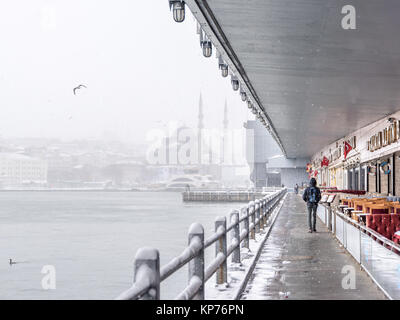 Unbekannter Mann gehen unter der Galatabrücke an einem verschneiten Tag im Winter. Neue Moschee ist auf dem Hintergrund. Istanbul, Türkei, 07. Januar 2017 Stockfoto