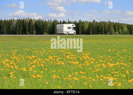 Weiß Reisemobil auf der Straße im Frühjahr mit einer Wiese von Löwenzahn auf der Vorderseite. Konzentrieren Sie sich auf das Fahrzeug. Stockfoto