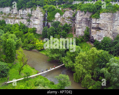 Brücke zu einem großen Berg, ein Foto von der Höhe: eine felsige Schlucht, unten am Fluss, eine dünne Brücke über den Türmen gedehnt wird, Touristen mit ruc Stockfoto