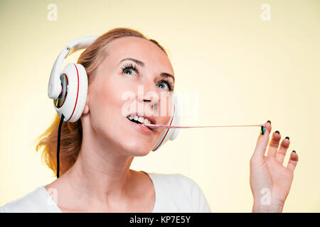 Blonde Mädchen mit Kopfhörer Sprengen eine Blase von Gummi auf gelbem Hintergrund Stockfoto