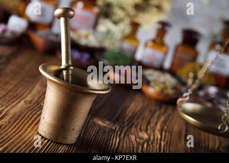 Natürliche Medizin Hintergrund. Messing Mörser, Flaschen und Skala. Rustikale Tabelle. Verschiedene trockene Kräuter in Schalen. Bokeh. Stockfoto