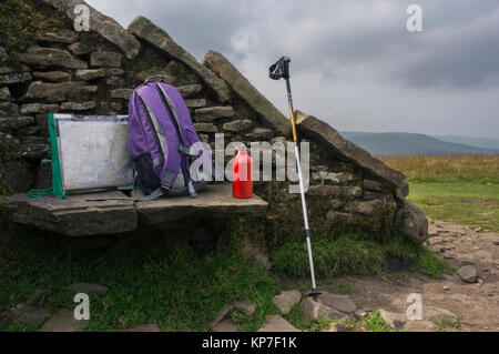 Stein Windschutz Tierheim & Sitz auf dem Gipfel der Whernside, mit Karte in den Halter, Rucksack, rot Flasche Wasser & Trekking Pol - Yorkshire Dales, England, UK. Stockfoto