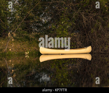 Fast perfekte Reflektion einer Banane gelb Kanu auf einem Teich mit Bäumen und Bürste Hintergrund Stockfoto