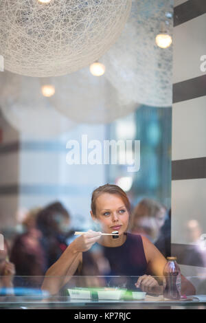 Hübsche, junge Frau Sushi essen in einem Restaurant, in der Mittagspause, genießen das Essen, Pausen für eine Weile aus Ihrem beschäftigten Corporate/Büro leben (Farbe getonte Bild) Stockfoto