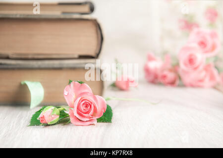 Zwei alte Bücher über Holz- Tabelle unter ziemlich kleine rosa Rosen, Platz für Ihre Begrüßung Text oder Bildunterschrift. Flache DOF, konzentrieren sich auf die Blume. Stockfoto