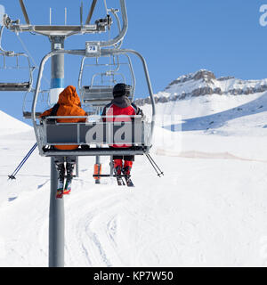 Zwei Skifahrer gehen auf der Sesselbahn und verschneite Skipiste bei Sun winter Tag. Kaukasus, Georgien, Region Gudauri. Stockfoto