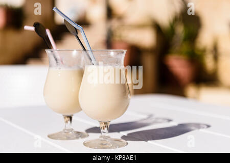 Zwei Gläser Pina Colada mit Strohhalm und Getränke Rührer auf einer Terrasse Tisch in der Sonne. Stockfoto