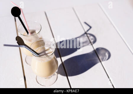 Zwei Gläser Pina Colada mit Strohhalm und Getränke Rührer auf einer Terrasse Tisch in der Sonne. Stockfoto