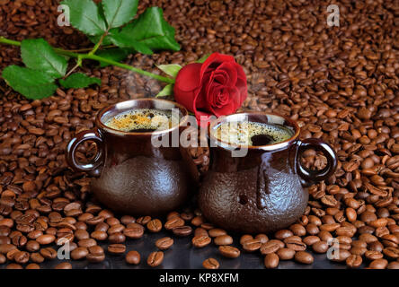 Zwei Tassen schwarzen Kaffee auf dem Hintergrund von Kaffeebohnen und eine rote Rose. Stockfoto