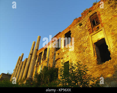 Die Ruinen einer alten Festung mit leeren Fenster, Mauerwerk, Spalten sind farbige Durch die Strahlen der Sonne in Orange. Stockfoto