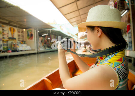 Junge hübsche Frau Touristen sitzen auf dem Fluss Boot mit Kamera Aufzeichnung lokale Anbieter anzeigen Landschaft während Thailand Reisen in Damnoen Saduak Stockfoto