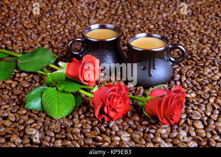 Drei rote Rosen und zwei Tassen Kaffee mit Milch auf dem Hintergrund von der Kaffeebohnen. Stockfoto