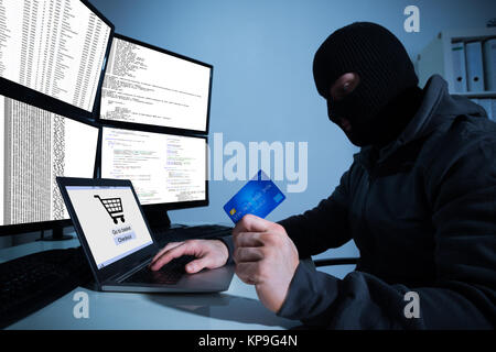 Hacker Holding Kreditkarte während mit Laptop auf dem Schreibtisch Stockfoto