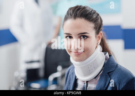 Junge lächelnde Patienten im Krankenhaus mit zervikaler Kragen unterstützen und Ärzte arbeiten auf dem Hintergrund Stockfoto