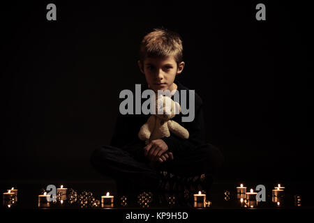 Junge mit Teddybär sitzt auf dem Boden mit Kerzen Stockfoto