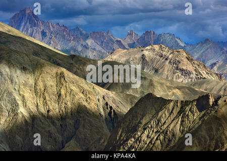 Lamayuru Bergketten, von den Strahlen der untergehenden Sonne beleuchtet, leuchtend gelbe Streifen und dunklen, Gipfeln im Hintergrund hingewiesen, den Himalaya. Stockfoto