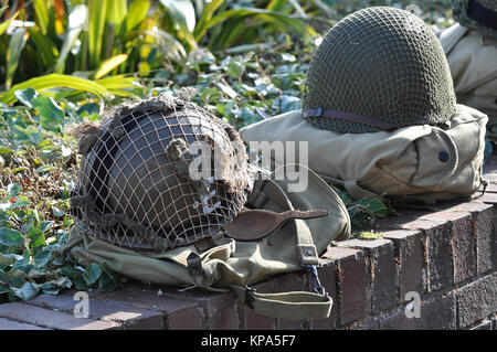 Helme und Packungen der US Army aus dem zweiten Weltkrieg, die an einer Wand bei einem Gedenkgottesdienst für Veteranen des D Day angebracht wurden. Gedenken. Ehrung. Kampfausrüstung Stockfoto